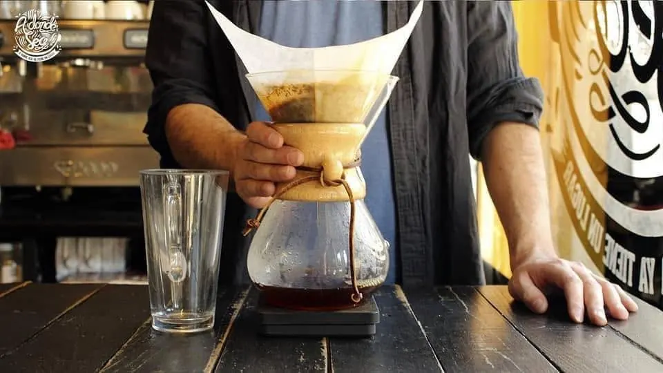 Barista preparando café en Chemex frente a la pared con el logo